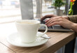 Cup of coffee on the table and hands of a girl working at a laptop in cafe. Work online. Close-up. Selective focus.