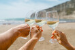 Close-up of friends' hands clinking glasses of white wine on the beach
