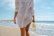 Young woman holds bottle of white wine and glasses on a sunny beach