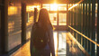 A female student walking through the school corridor, bathed in the warm glow of the sun streaming through nearby windows. Her confident stride and the soft shadows cast along the