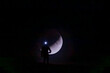 © ADDICTIVE STOCK - A stunning silhouette of a lone individual wearing a headlamp, standing before a backdrop of the crescent moon in a dark, serene night sky