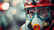 A man in a red helmet and goggles is wearing a mask. He looks serious and focused. The scene appears to be set in a dangerous or hazardous environment, such as a construction site or a chemical plant