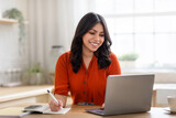 Fototapeta  - Woman writing and smiling at laptop at home