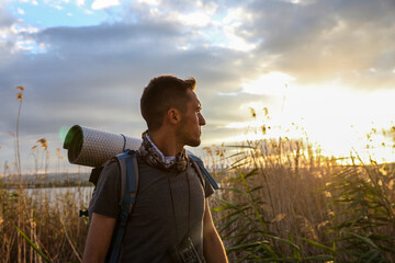 Wall Mural - A man is walking through a field with a backpack on. Scene is peaceful and serene, as the man is surrounded by nature