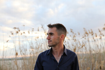 Wall Mural - A man in a white shirt stands in a field of tall grass. The sky is cloudy and the sun is setting