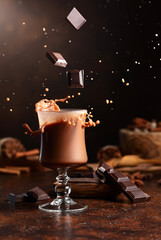 Wall Mural - Pieces of dark chocolate fall into a glass of cocoa drink.