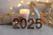 Happy new year 2025 postcard. Golden digits in front of Christmas lights, candles, gift box. White wooden background. Copy space for greeting text