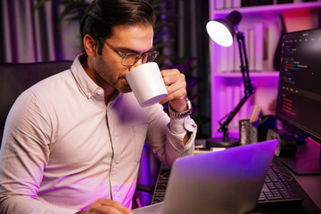 Smart IT developer drinking coffee cup while working in software development coding on pc screen, presenting program application update online website database at neon lighting cyber office. Surmise.