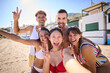 © CarlosBarquero - Portrait of a group of cheerful multiracial young gen z friends taking a selfie on the beach looking at camera, smiling and having fun together. People enjoying summer leisure time and holidays travel