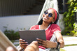 African American young woman relaxing in hammock at home, holding tablet