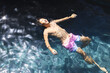 © Wavebreak Media - A teenage Asian boy is floating in a pool outside at home, wearing a pink swim bottom, copy space