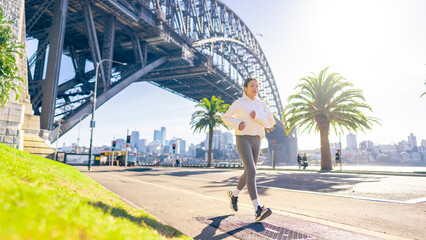 Wall Mural - Asian woman in sportswear listening to music with earphones and mobile phone app jogging workout exercise at city street in the morning. Healthy care motivation sport training and running concept.