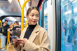 © CandyRetriever  - Asian woman using mobile phone and listening to the music on earphones during travel on train in the city. Attractive girl enjoy urban lifestyle in the city with using wireless technology on device.