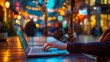Defocused cityscape with a person typing on a laptop in a bustling outdoor cafe. The blurred lights and movement of people in the background represent the hustle and bustle of traditional .