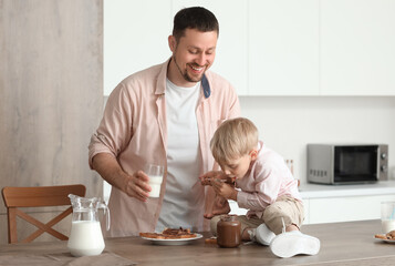 Poster - Little boy with his father eating chocolate paste toasts and drinking milk in kitchen