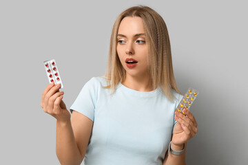 Wall Mural - Young woman with blisters of vitamin A pills on light background