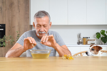 Wall Mural - Mature man with dog preparing steam inhalation at table in kitchen