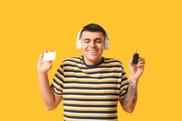 Poster - Young man in headphones with blank driving license and car key on yellow background