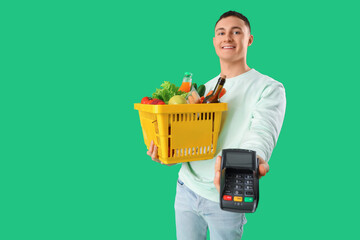 Sticker - Young man with full shopping basket and payment terminal on green background