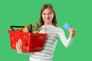 Poster - Young woman with full shopping basket and credit card on green background