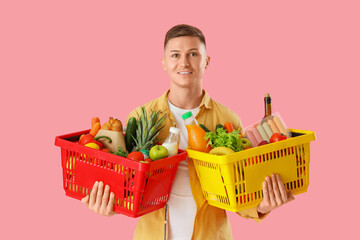 Wall Mural - Young man with full shopping baskets on pink background