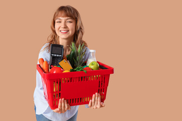 Wall Mural - Young woman with full shopping basket and payment terminal on beige background