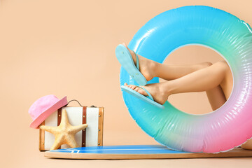 Wall Mural - Young woman with surfboard, inflatable ring and suitcase on beige background. Summer vacation concept