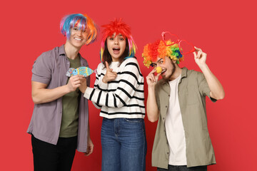 Wall Mural - Young shocked friends in funny disguise with paper fishes on red background. April fool's day celebration