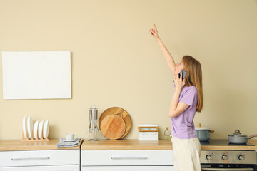 Wall Mural - Young woman with mold on wall talking by mobile phone in kitchen