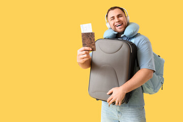 Canvas Print - Young happy man with suitcase, headphones, passport and travel pillow on yellow background