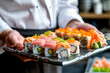 A sushi chef is holding a tray of sushi rolls, including some with avocado
