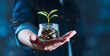 A person is holding a jar with a plant inside and coins