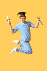 Wall Mural - Happy male medical graduate student with diploma and stethoscope jumping on yellow background