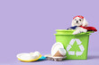 Cute little dog in eco superhero costume with trash bins and garbage on lilac background