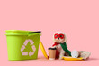 Cute little dog in eco superhero costume with trash bins and garbage on pink background