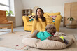 Young woman in headphones listening to music with cute poodle on pet bed at home