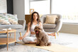 Sporty young woman with cute poodle meditating at home