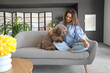 Young woman with funny poodle sitting on sofa at home