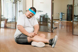 Fototapeta  - Portrait of young plus size overweight man holding a knee suffering from an injury in a gym