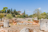 Fototapeta Desenie - Sunny view of ancient ruins with a distant view of Hephaistos temple surrounded by lush greenery, in Athens, Greece