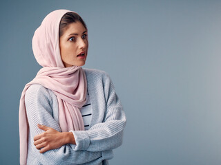 Poster - Shock, hijab and muslim woman with arms crossed in studio for surprise, wow or omg reaction on blue background. Islam, amazed and Arab person with wtf expression for gossip, fake news or announcement