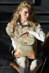 Wall Mural - beautiful curly blond hair woman posing with a leather backpack