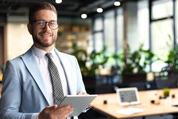 Wall Mural - Modern business man in formalwear using digital tablet while standing near window in the office