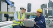 © HarryKiiM Stock - engineers manager and worker sitting on rooftop review plans on a laptop while on a construction site with high-rise buildings, indicating their different roles and responsibilities on the project