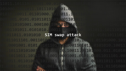 Sim swap attack text in foreground screen, anonymous hacker hidden with hoodie in the blurred background. Vulnerability text in binary system code on editor program.