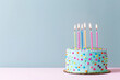 © CozyDigital - Birthday cake with candles stands on table on blue background with copy space.