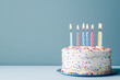 © CozyDigital - Birthday cake with candles stands on table on blue background with copy space.