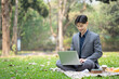 © Prathankarnpap - Portrait of smiling businessman using laptop on blanket at public park