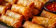 A close-up view of delicious, perfectly fried spring rolls served with a dipping sauce, highlighting the golden crispy texture
