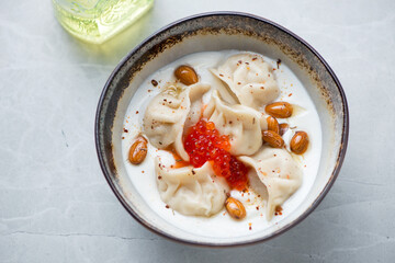 Wall Mural - Bowl of white yogurt with vareniki dumplings and red caviar, horizontal shot on a light-grey granite background, elevated view